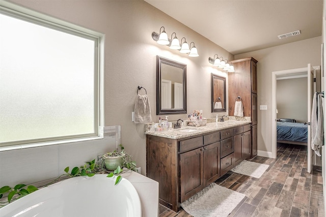 bathroom with visible vents, double vanity, wood finished floors, a soaking tub, and a sink