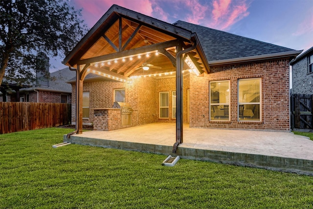 rear view of house with ceiling fan, a yard, brick siding, and a fenced backyard