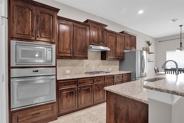 kitchen featuring a sink, stainless steel appliances, visible vents, under cabinet range hood, and tasteful backsplash