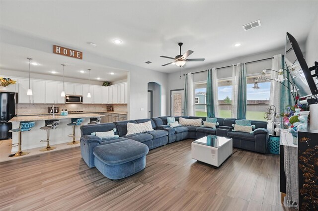 living area with visible vents, light wood-style floors, ceiling fan, recessed lighting, and arched walkways