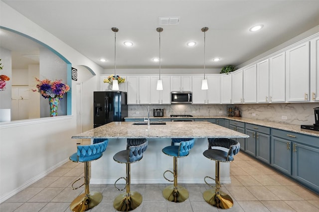 kitchen featuring a sink, stainless steel microwave, backsplash, and black fridge