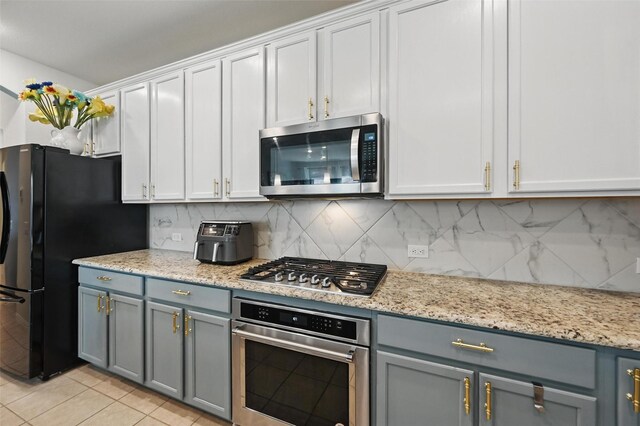 kitchen with gray cabinets, backsplash, light stone countertops, stainless steel appliances, and light tile patterned flooring