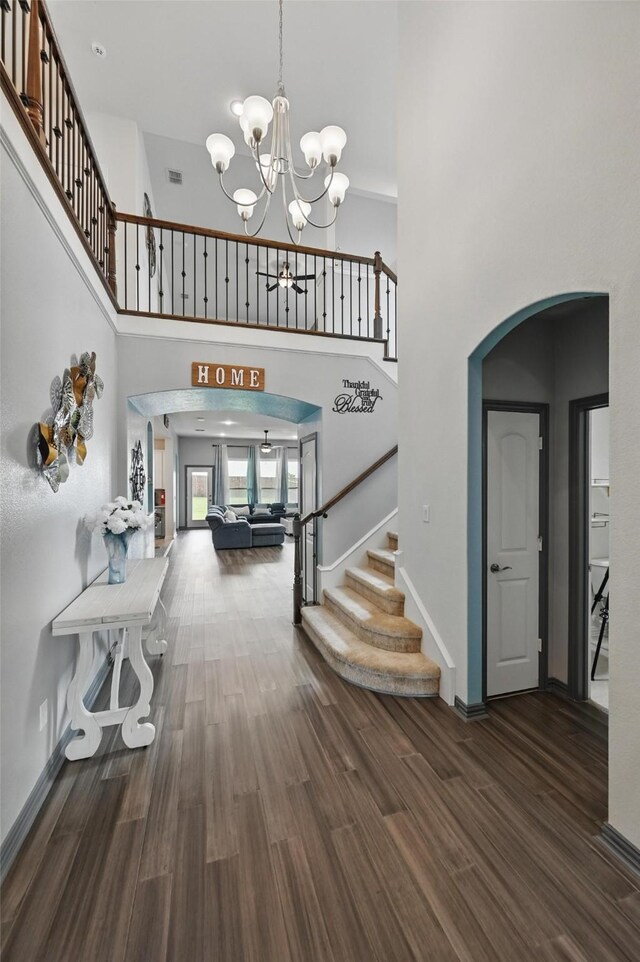 foyer entrance with stairs, a high ceiling, arched walkways, dark wood finished floors, and a notable chandelier