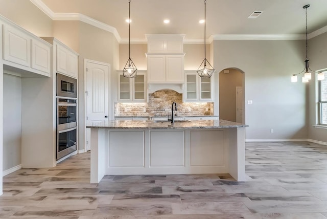 kitchen with arched walkways, stainless steel appliances, white cabinetry, visible vents, and ornamental molding