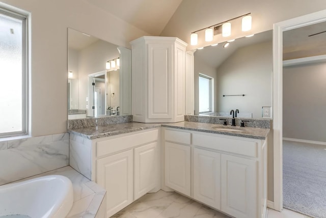 bathroom featuring double vanity, marble finish floor, a bath, a sink, and vaulted ceiling