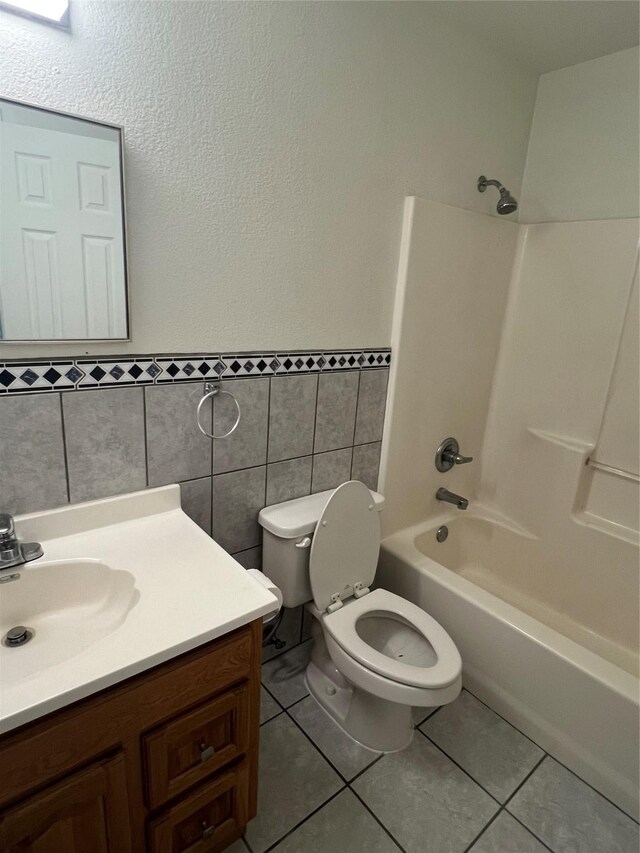 bathroom featuring tile patterned flooring, vanity, bathtub / shower combination, toilet, and tile walls