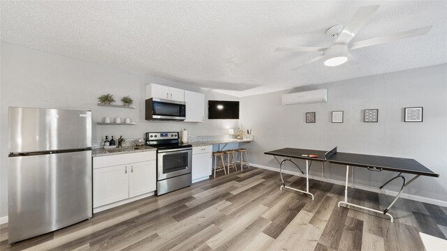 kitchen featuring open shelves, a wall mounted air conditioner, white cabinets, light wood-style flooring, and stainless steel appliances