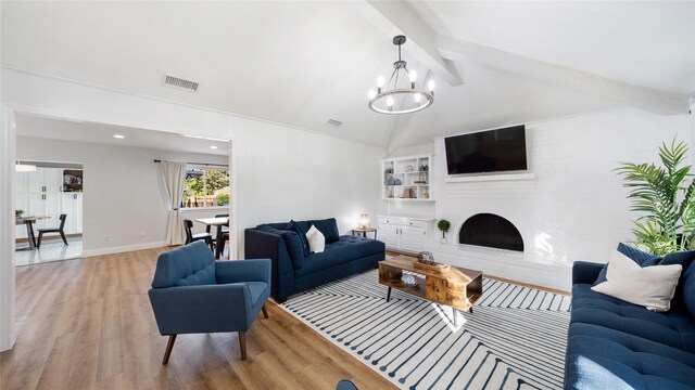 living room with an inviting chandelier, visible vents, wood finished floors, vaulted ceiling with beams, and a fireplace with raised hearth