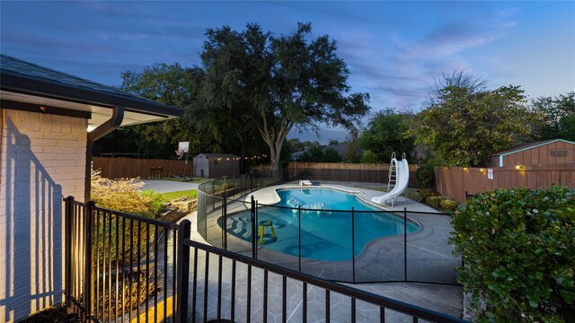 view of pool featuring a patio area, a fenced in pool, a fenced backyard, a storage unit, and a water slide