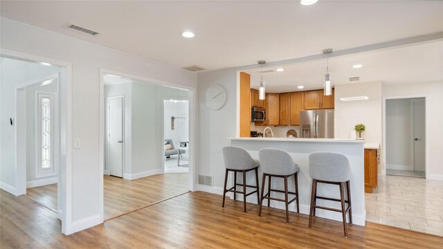 kitchen featuring a kitchen breakfast bar, brown cabinetry, stainless steel appliances, and visible vents