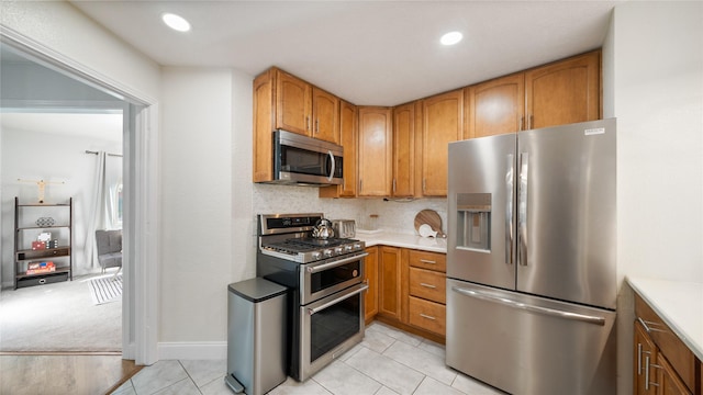 kitchen featuring light countertops, brown cabinetry, stainless steel appliances, baseboards, and light tile patterned floors