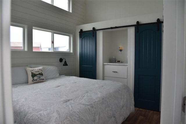bedroom with a barn door, dark wood finished floors, and wooden walls
