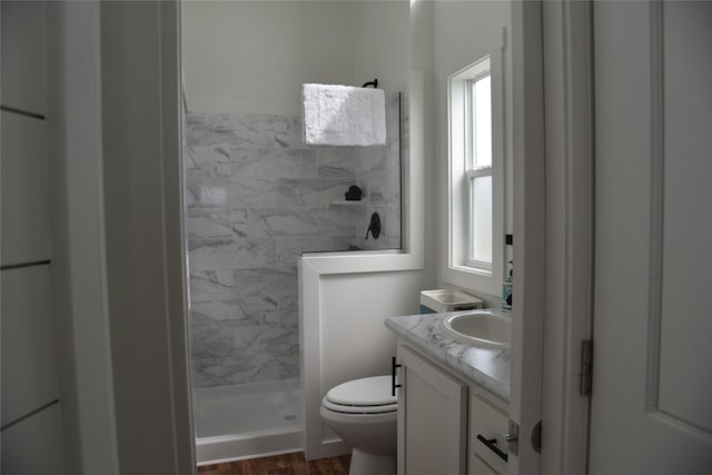 full bathroom featuring wood finished floors, toilet, tiled shower, and vanity