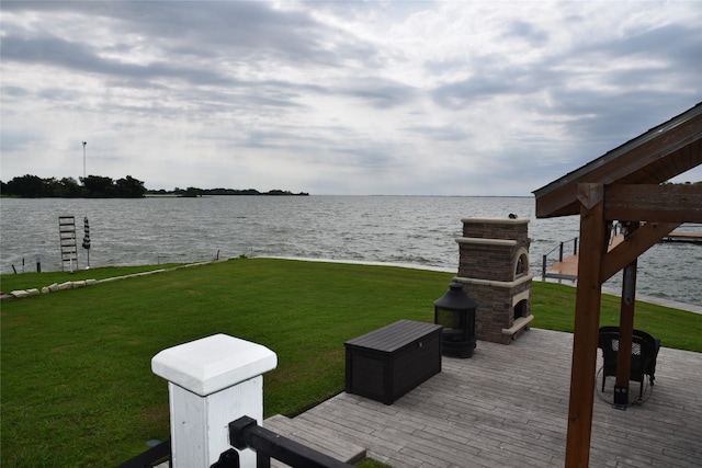 exterior space featuring a lawn, a water view, and an outdoor stone fireplace