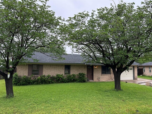 ranch-style home with roof with shingles, a garage, brick siding, a front lawn, and concrete driveway