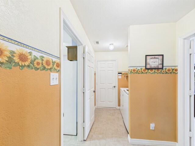 hallway with visible vents, light tile patterned flooring, and washer and clothes dryer