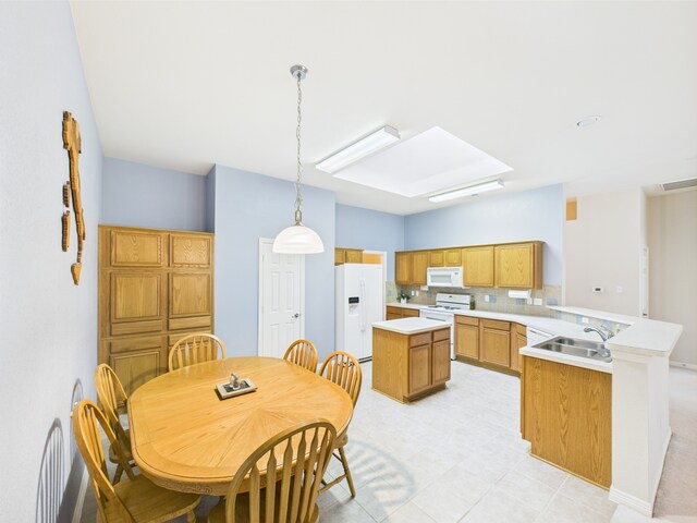 kitchen with a peninsula, a kitchen island, white appliances, light countertops, and a sink