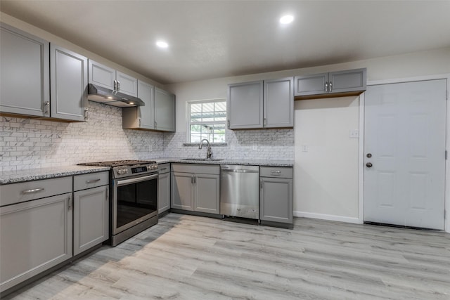 kitchen featuring gray cabinets, appliances with stainless steel finishes, a sink, under cabinet range hood, and light wood-style flooring