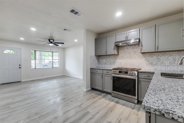 kitchen featuring gas range, a sink, under cabinet range hood, and gray cabinetry