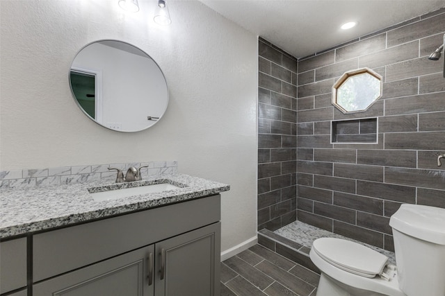 full bathroom featuring wood finish floors, a tile shower, vanity, toilet, and baseboards
