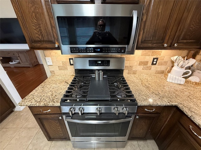 interior space with stainless steel appliances, dark brown cabinetry, light stone counters, and tasteful backsplash