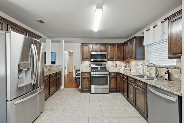 4610 Bluebird Ln, Mansfield, TX 76063 - kitchen featuring appliances with stainless steel finishes, a sink, decorative backsplash, light stone countertops, and arched walkways