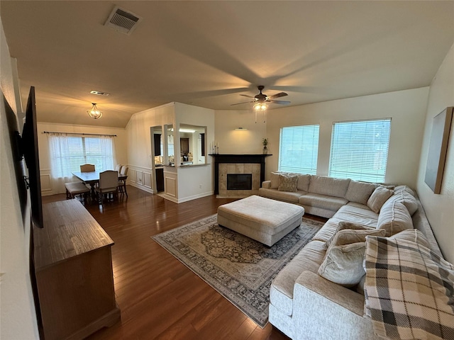 living room featuring dark wood-style flooring, ceiling fan, visible vents, and a tile fireplace