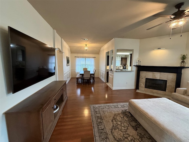 living room with dark wood-type flooring, ceiling fan, and a tile fireplace