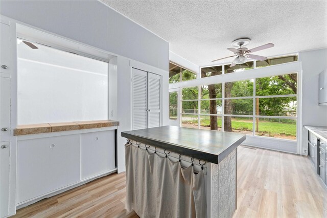 kitchen with a textured ceiling, ceiling fan, light wood-style flooring, and white cabinets