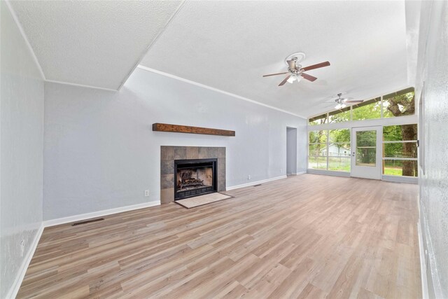 unfurnished living room with visible vents, a tiled fireplace, a ceiling fan, wood finished floors, and vaulted ceiling