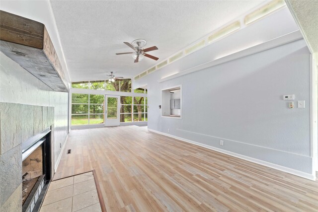 unfurnished living room with a ceiling fan, a textured ceiling, a tiled fireplace, light wood-type flooring, and baseboards