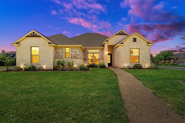 view of front facade with a shingled roof, a front yard, and stone siding