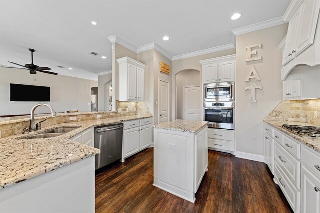 kitchen featuring ceiling fan, appliances with stainless steel finishes, a sink, arched walkways, and decorative backsplash