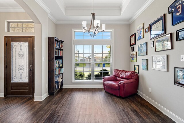 living area with crown molding, dark wood finished floors, baseboards, a chandelier, and a tray ceiling