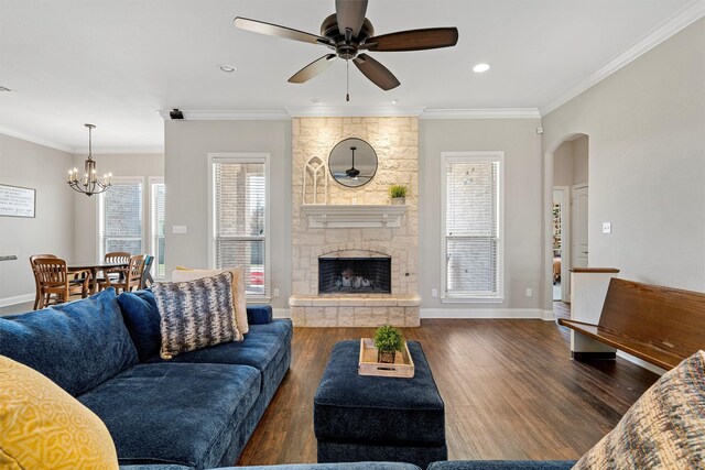living room with crown molding, arched walkways, a fireplace, wood finished floors, and ceiling fan with notable chandelier