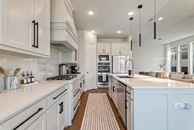 kitchen featuring decorative backsplash, a sink, premium range hood, light countertops, and an island with sink