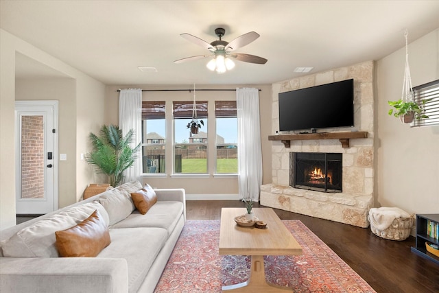 living room featuring ceiling fan, a stone fireplace, and wood finished floors