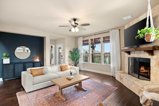 living room with wood finished floors, ceiling fan, a stone fireplace, and visible vents