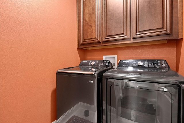 laundry area featuring washing machine and clothes dryer, a textured wall, and cabinet space