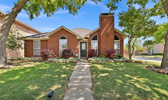 view of front facade with a shingled roof, a chimney, a front lawn, and brick siding