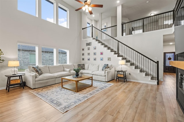 living area with a ceiling fan, light wood-style flooring, a high ceiling, and stairway