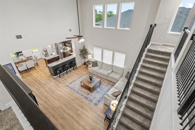 living area featuring visible vents, a towering ceiling, wood finished floors, stairway, and a ceiling fan