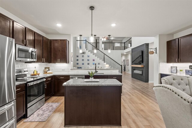 kitchen featuring a peninsula, a kitchen island, open floor plan, a sink, and appliances with stainless steel finishes