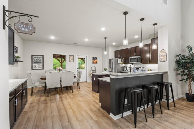 kitchen with dark brown cabinets, appliances with stainless steel finishes, a breakfast bar, light wood-style floors, and a peninsula