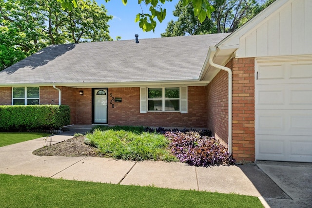 ranch-style home with roof with shingles, an attached garage, and brick siding