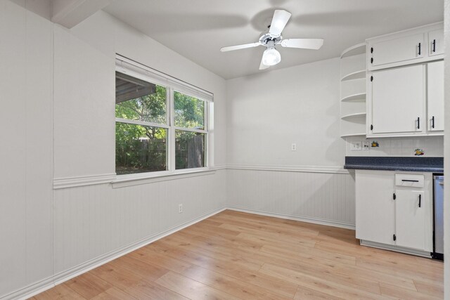 interior space featuring light wood-style flooring, ceiling fan, and a wainscoted wall