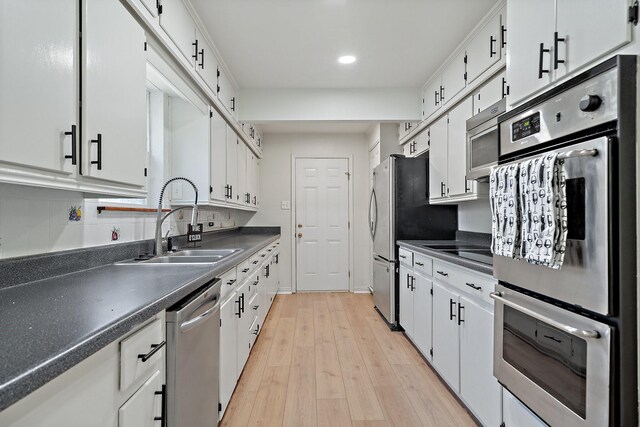 kitchen with a sink, dark countertops, stainless steel appliances, and white cabinetry