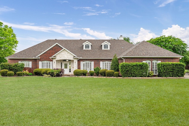 cape cod home featuring brick siding, a front yard, a chimney, and roof with shingles