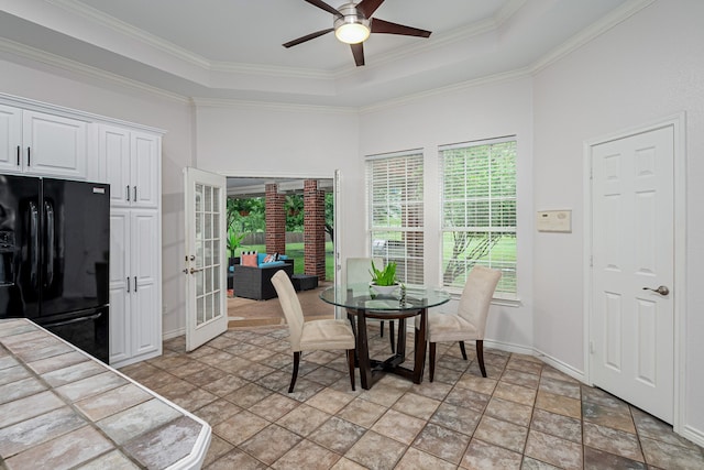 dining space with stone finish floor, ceiling fan, french doors, crown molding, and a raised ceiling