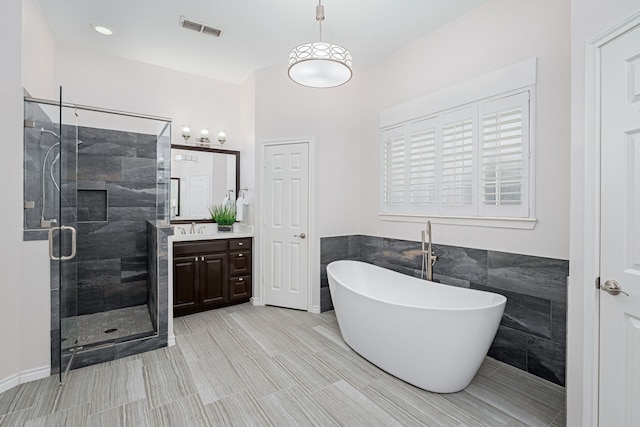 bathroom with vanity, tile walls, visible vents, a soaking tub, and a stall shower